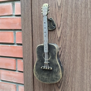 Può includere: Una maniglia per porta a forma di chitarra nera e dorata con una finitura usurata.