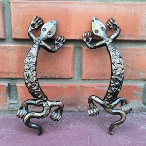 Puede incluir: Dos tiradores de puerta de metal negro en forma de lagarto con acabado texturizado. Los lagartos están en posición enroscada con las colas enroscadas.