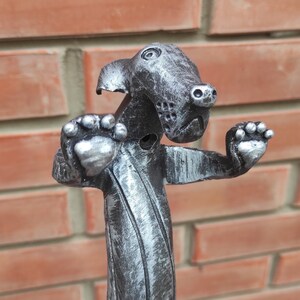 May include: A silver metal sculpture of a dog with its paws raised in the air. The dog is stylized with a textured, striped body and a detailed face.