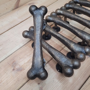 Puede incluir: Un juego de ocho tiradores de puerta con forma de hueso en un acabado bronce oscuro. Los tiradores están hechos de metal y tienen una superficie texturizada.