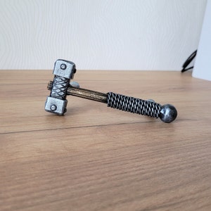 May include: A silver and brown metal hammer with a braided handle. The hammer has a textured head and a round end.