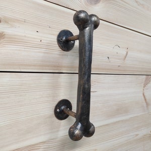 Peut inclure: Une poignée de porte en métal noir en forme d'os avec des extrémités arrondies. La poignée est montée sur une surface en bois.