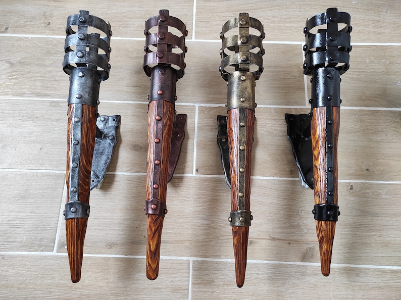 May include: Four wall-mounted torch sconces with a wood and metal design. The sconces are in different finishes: silver, copper, gold, and black.