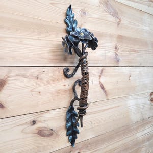 May include: A decorative door handle made of metal, shaped like a flower with leaves. The handle is painted in shades of blue and brown.