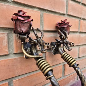 Op de afbeelding: Twee decoratieve wandhaken in de vorm van draken met een roos erop. De draken zijn gemaakt van metaal en hebben een gouden afwerking. De rozen zijn rood en hebben een textuur.