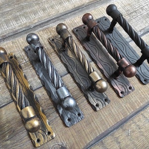 Może przedstawiać: Pięć różnych metalowych klamki do drzwi z wzorem skręconej liny. Klamki są w różnych wykończeniach, w tym czarnym, srebrnym i złotym.