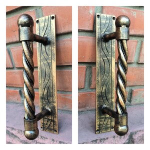 May include: A gold-toned door handle with a twisted rope design. The handle is attached to a rectangular plate with a decorative wave pattern.