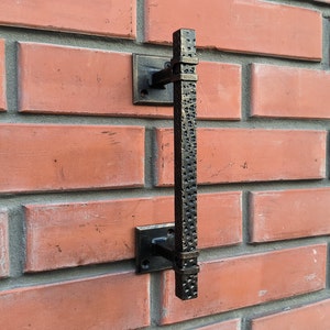 May include: Black metal door handle with a textured finish mounted on a brick wall.
