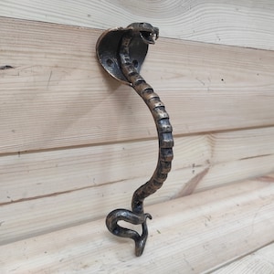 Peut inclure: Une poignée de porte décorative en forme de cobra. La poignée est en métal et a une finition bronze foncé.