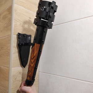 May include: A black metal wall-mounted torch with a wooden handle. The torch has a decorative metal design with rivets and a black finish. The handle is made of wood with a brown stain.