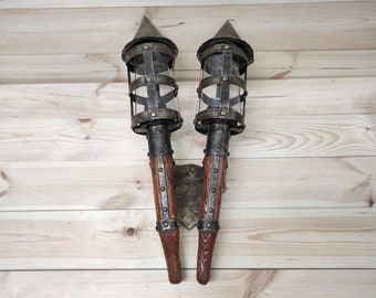 May include: A pair of wall-mounted, metal and wood torch sconces with glass panels. The sconces are in a rustic style and have a dark brown finish.