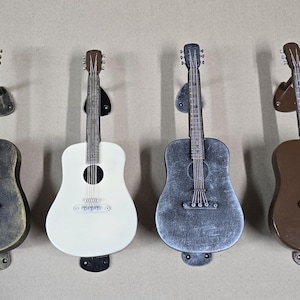 May include: Four acoustic guitars with different finishes, hanging on wall mounts. The guitars are black, white, brown, and silver.