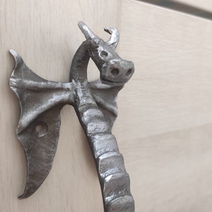 Op de afbeelding: Een zilveren drakenvormige deurknop met een textuur. De knop is ontworpen met een drakenkop en vleugels.