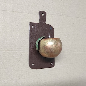 May include: A brown wooden cutting board with a metal apple-shaped hook. The apple is gold with a green leaf.
