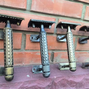 May include: Four vintage-style safety razors in various metallic finishes, mounted on a brick wall. The razors have textured handles and are attached to the wall with small metal brackets. The colors range from gold to bronze.