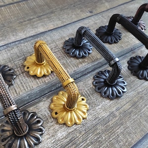 Könnte beinhalten: Vier dekorative Schranktürgriffe mit einem geflochtenen Seil-Design. Die Griffe sind in Gold, Schwarz und Silber ausgeführt.