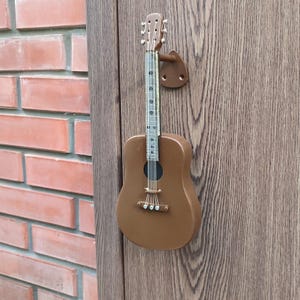 Può includere: Una maniglia per porta in legno marrone a forma di chitarra con piroli argentati e un ponte argentato. La maniglia è montata su una porta in legno.
