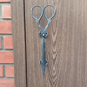 Könnte beinhalten: Ein silberner Türgriff aus Metall in Form einer Schere. Der Griff ist an einer Holztür montiert.