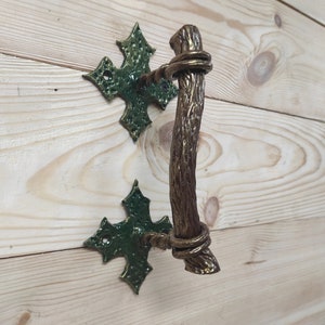 May include: A decorative door handle with a twisted branch design and green metal accents. The handle is made of metal and has a rustic look.