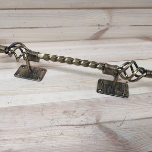 May include: Ornate, antique-style metal curtain rod with a twisted center and decorative finials. The rod is a bronze color with a distressed finish, mounted on rectangular plates. A decorative home decor item.