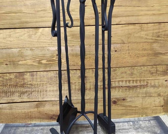 Könnte beinhalten: Schwarzes Kaminwerkzeug-Set aus Metall mit Ständer. Das Set enthält einen Schürhaken, eine Schaufel, eine Zange und eine Bürste. Die Werkzeuge sind alle verdreht und haben dekorative Schlaufen oben.