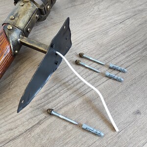 May include: A wooden and metal wall mount with a black metal plate and a white wire. The mount is accompanied by several plastic wall anchors and screws.