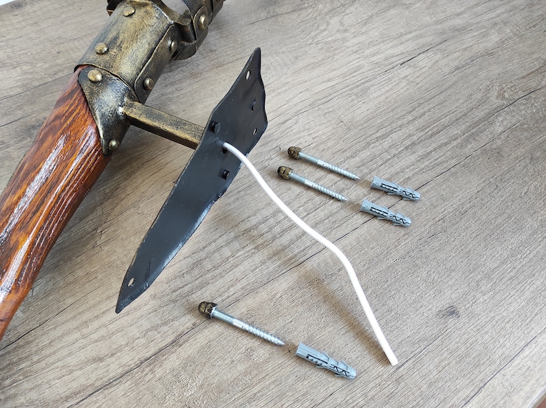May include: A wooden and metal wall mount with a black metal plate and a white wire. The mount is accompanied by several plastic wall anchors and screws.