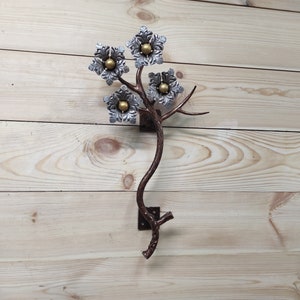 Könnte beinhalten: Eine Wandskulptur aus Metall in Form eines stilisierten Baumes mit fünf silbernen Blüten mit goldenen Zentren. Der Baum ist an einer Holzwand befestigt.