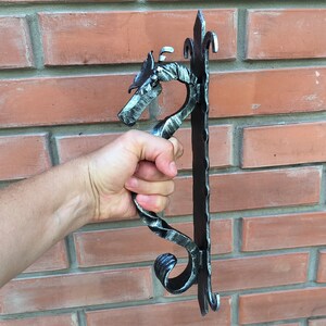 Puede incluir: Una manilla de puerta de metal negro con un diseño de dragón. La manilla está hecha de metal retorcido y tiene un diseño decorativo de volutas.
