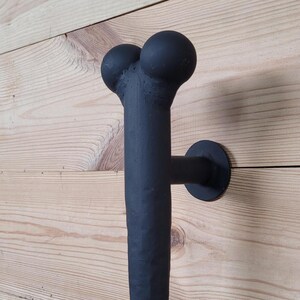 Peut inclure: Poignée de porte en métal noir en forme d'os avec des extrémités arrondies. La poignée est fixée à un mur en bois.