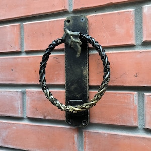 Puede incluir: Un anillo para toalla de metal negro con un diseño retorcido de color dorado. El anillo está montado en una placa de metal negro con un diseño de hoja.