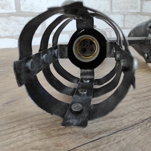 May include: A black metal cage light fixture with a round, open design. The fixture has a standard light bulb socket and is designed for wall mounting.
