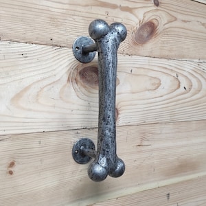 Puede incluir: Un tirador de puerta de hueso plateado con un acabado texturizado. El tirador está montado en una superficie de madera.