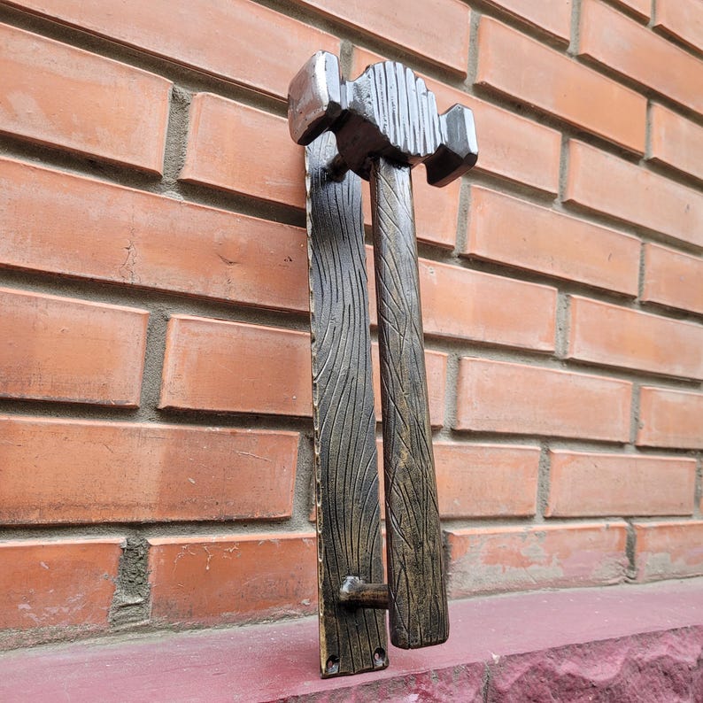 Puede incluir: Un juego de manijas de puerta decorativas con un dise&ntilde;o r&uacute;stico. Las manijas son de metal y presentan una textura de vetas de madera. La parte superior de la manija tiene forma de martillo. La combinaci&oacute;n de colores es una mezcla de plata y marr&oacute;n.