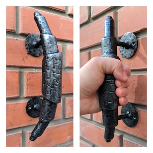 Puede incluir: Una manija de puerta de metal negro con un diseño único retorcido. La manija está montada en una pared de ladrillo.