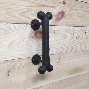 Puede incluir: Pomo de puerta de hueso negro de metal con acabado texturizado. El pomo está montado en una superficie de madera.