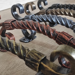 Op de afbeelding: Een set van vijf decoratieve metalen haken met een gedraaid ontwerp. De haken zijn in verschillende afwerkingen, waaronder koper, zwart en goud.