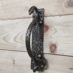 Könnte beinhalten: Ein dekorativer Türgriff in Form einer Schlange mit einer strukturierten, schwarzen Oberfläche und goldenen Akzenten. Der Griff ist an einer Holztür montiert.