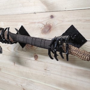 May include: A black metal axe holder shaped like a skeletal hand, mounted on a wooden wall. The axe has a brown wooden handle and a metal head.