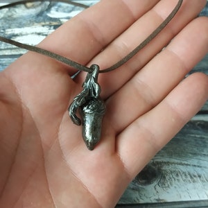 Pode incluir: Um colar com um pingente de bolota de prata em um cordão de couro marrom. A bolota é detalhada com um caule e folhas.