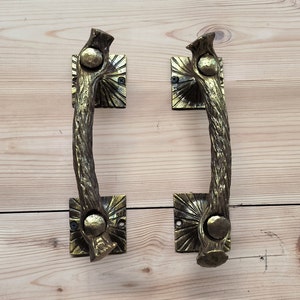 May include: A pair of antique-style door handles with a rustic, branch-like design. The handles are made of metal and have a gold finish. They are mounted on square plates with a sunburst pattern.