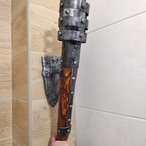 May include: A silver metal wall-mounted torch with a wooden handle. The torch has a decorative metal cage around the top and is mounted on a metal bracket.