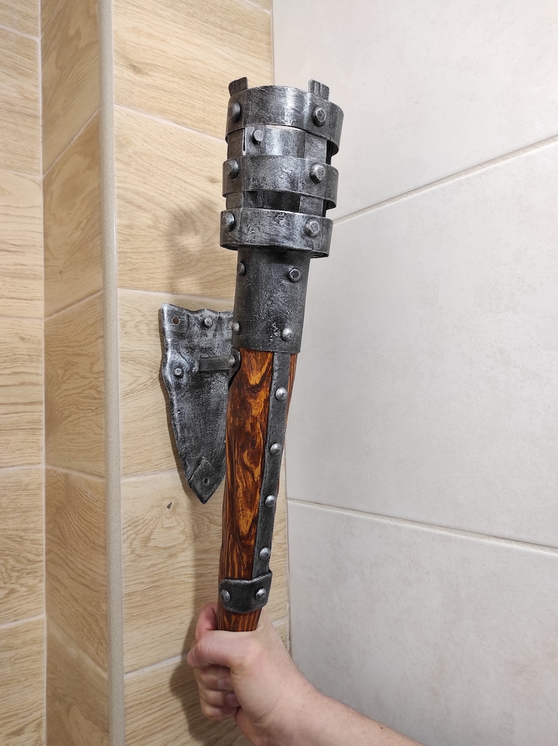 May include: A silver metal wall-mounted torch with a wooden handle. The torch has a decorative metal cage around the top and is mounted on a metal bracket.