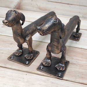 Könnte beinhalten: Zwei antike bronzene Dackel-Türgriffe mit einer patinierten Oberfläche. Die Griffe sind aus Metall und haben ein realistisches Hunde-Design.