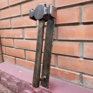 Puede incluir: Un juego de manijas de puerta decorativas con dise&ntilde;o de martillo. La manija es de madera marr&oacute;n oscuro con un acabado texturizado y detalles dorados. La cabeza del martillo es de un tono marr&oacute;n m&aacute;s oscuro.