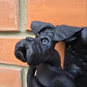 May include: Black metal sculpture of a dog with its head tilted to the side. The dog has a textured surface and appears to be made of cast iron.
