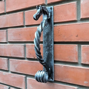 May include: A silver metal door knocker shaped like a horse's head with a twisted rope design. The knocker is mounted on a brick wall.