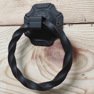 May include: Black metal door handle with a twisted ring pull and a decorative octagonal plate. The handle is mounted on a light wood surface.