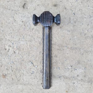 Puede incluir: Un martillo de bola negro y texturizado con una cabeza acanalada y un mango de madera tallada. El martillo est&aacute; dise&ntilde;ado para dar forma al metal y presenta una pena redondeada para extender remaches o dar forma al metal.