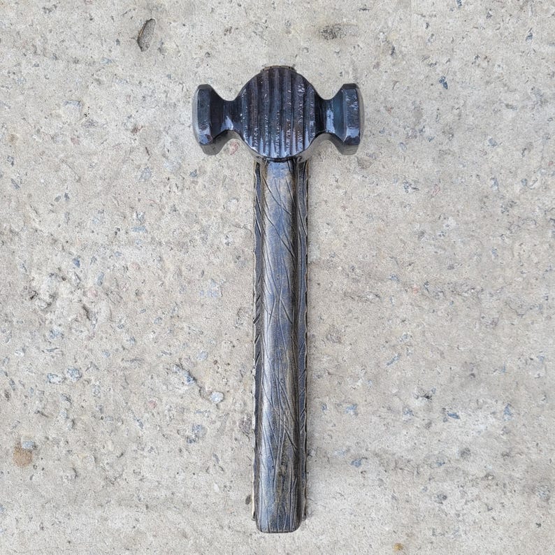 Puede incluir: Un martillo de bola negro y texturizado con una cabeza acanalada y un mango de madera tallada. El martillo est&aacute; dise&ntilde;ado para dar forma al metal y presenta una pena redondeada para extender remaches o dar forma al metal.